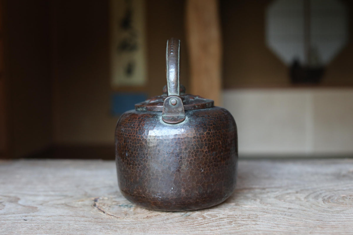An old, round, metal teapot with a textured surface sits on a wooden surface.