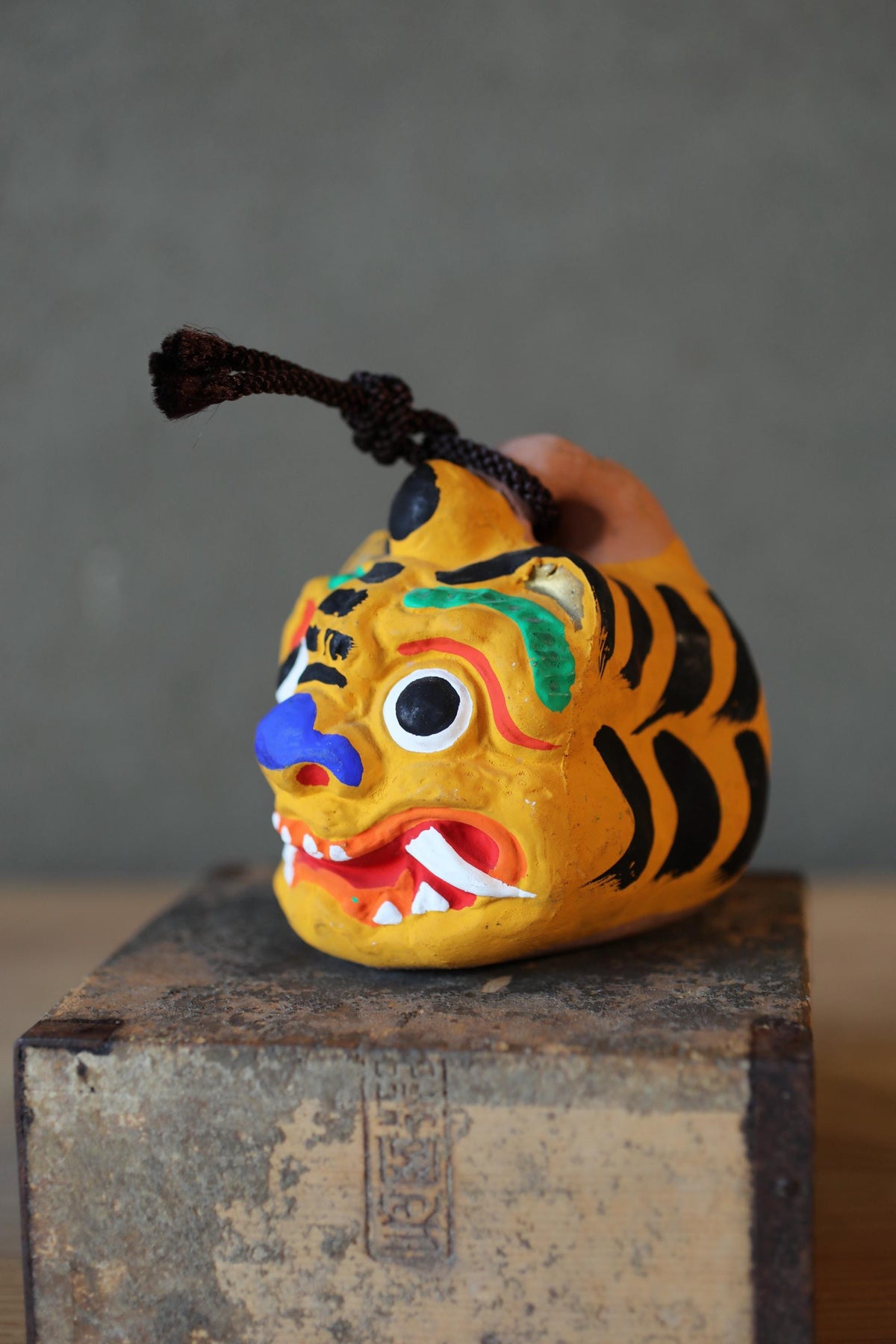 A colorful, painted figurine of a tiger's head is displayed on a wooden surface.