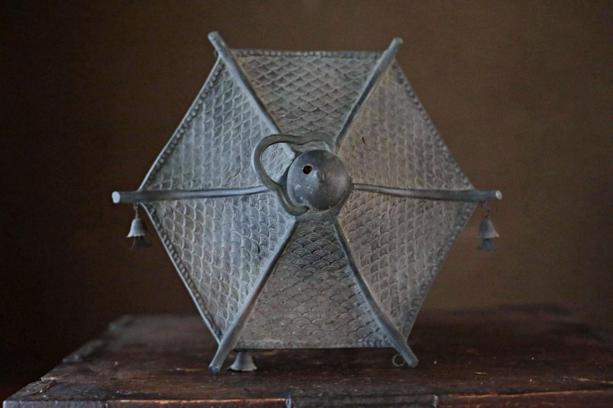 A metal lamp with a geometric patterned design, featuring a round base and a handle on top.