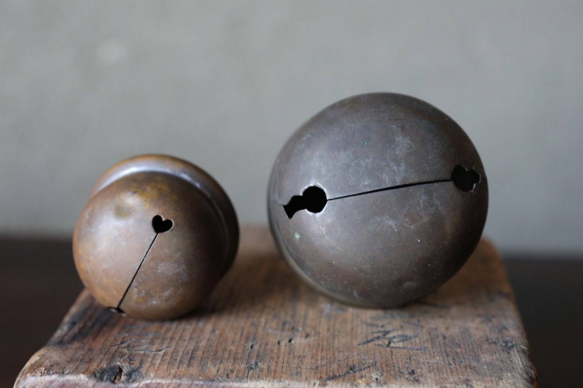 Two antique brass bells with holes in the center, one larger and one smaller, sit on a wooden surface.