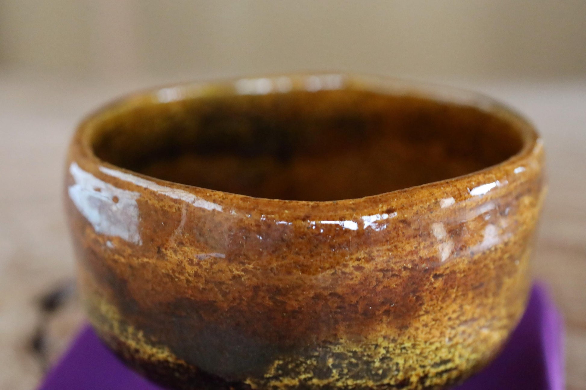 A close-up image of a ceramic bowl with a brown and orange color scheme, sitting on a purple surface.