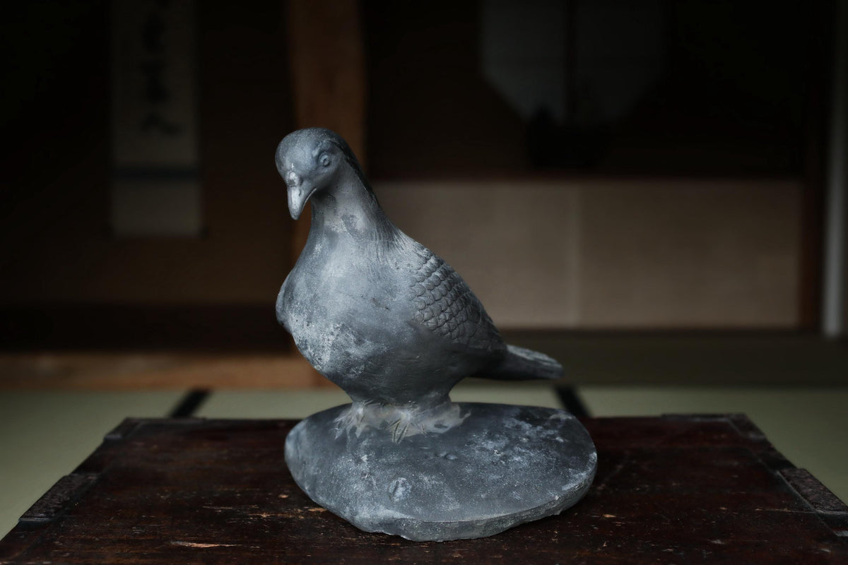 A gray metal bird statue perched on a wooden surface.