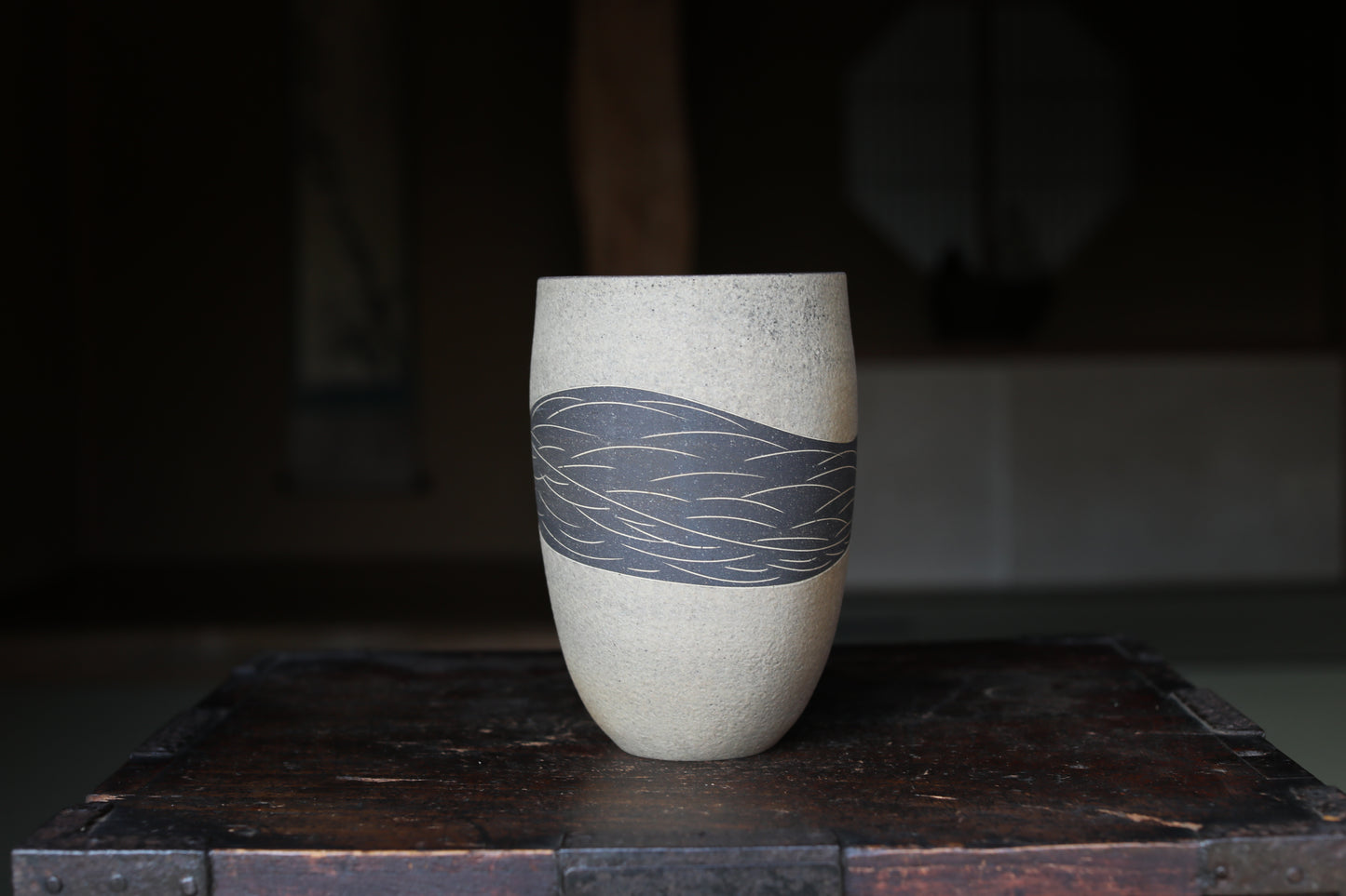 A white ceramic vase with a black wave design on it, placed on a wooden surface.