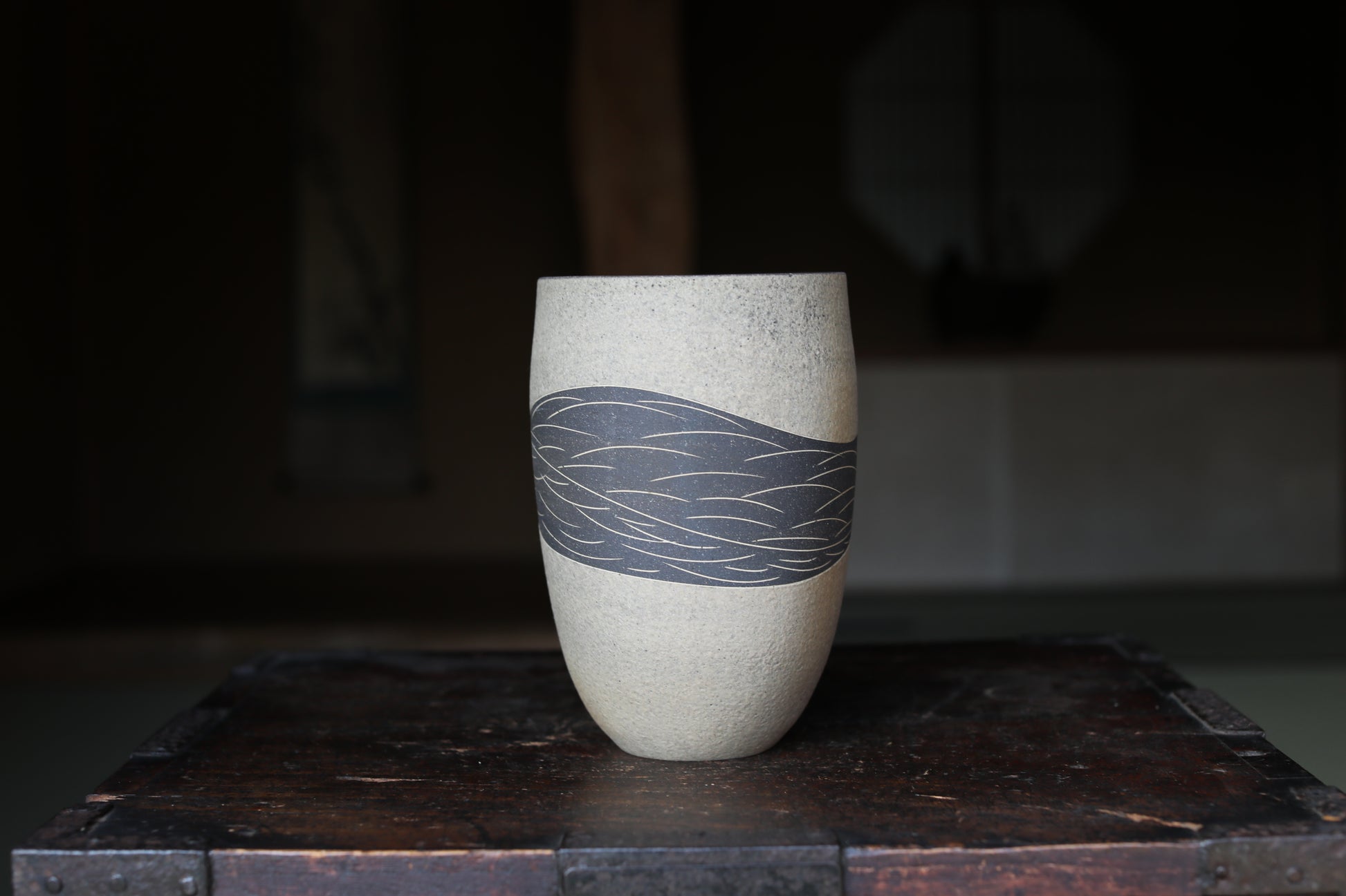 A white ceramic vase with a black wave design on it, placed on a wooden surface.