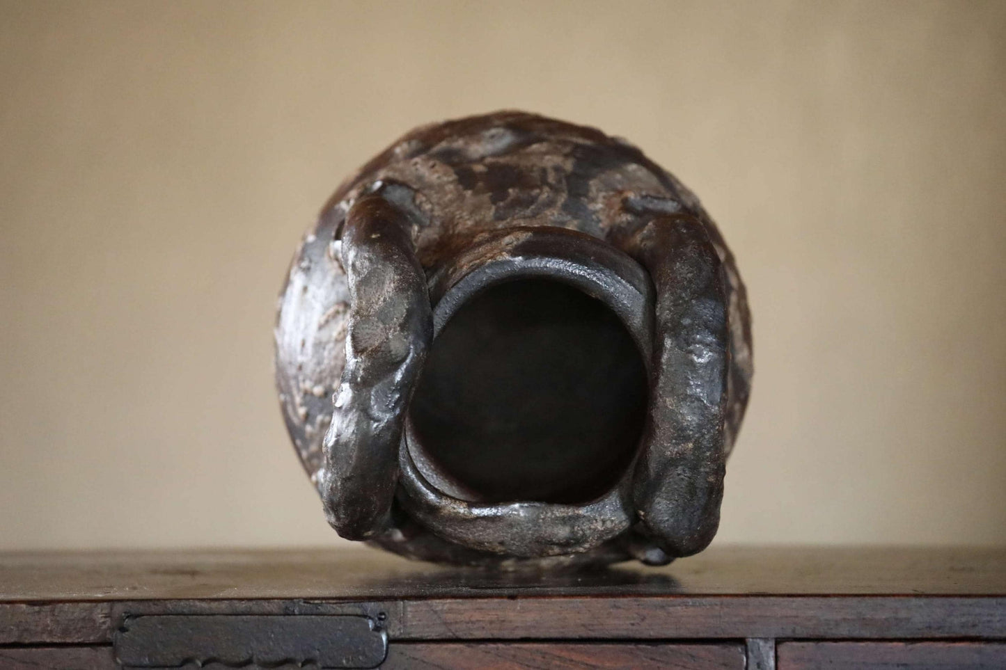 An old, rusted metal vase with a large, circular opening in the center, sitting on a wooden surface.