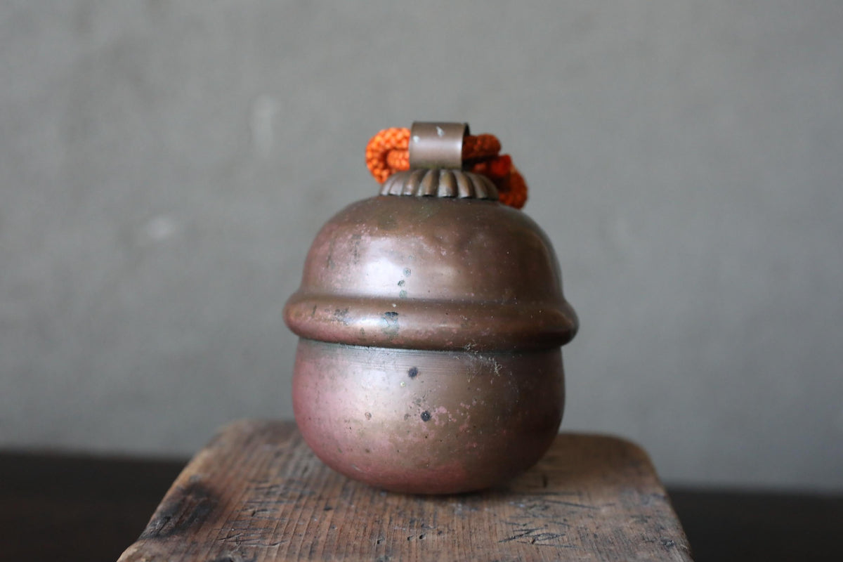 A round, metallic object with a small, orange-colored decoration on top, sitting on a wooden surface against a gray background.