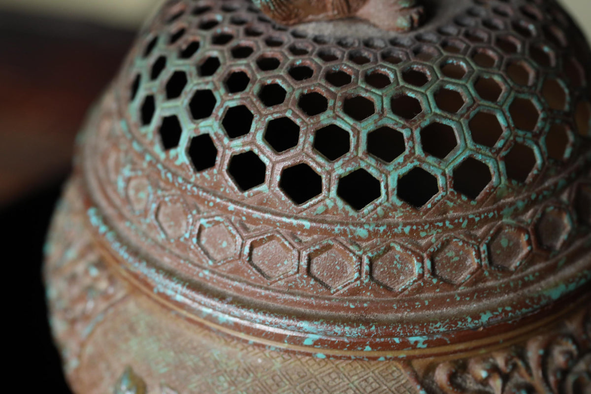 A close-up view of a metal incense burner with a textured surface and a pattern of hexagonal holes.