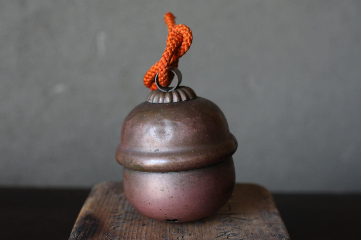 A round, metallic bell with a red string hanging from it, placed on a wooden surface against a gray background.