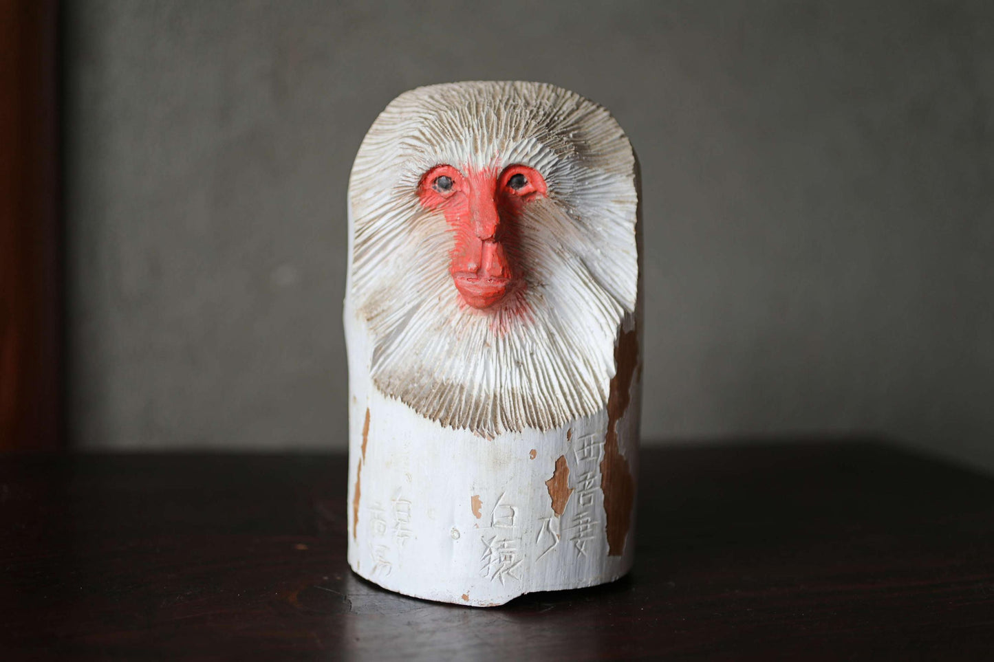 A wooden sculpture of a monkey's head with a red nose and white fur, sitting on a dark surface.