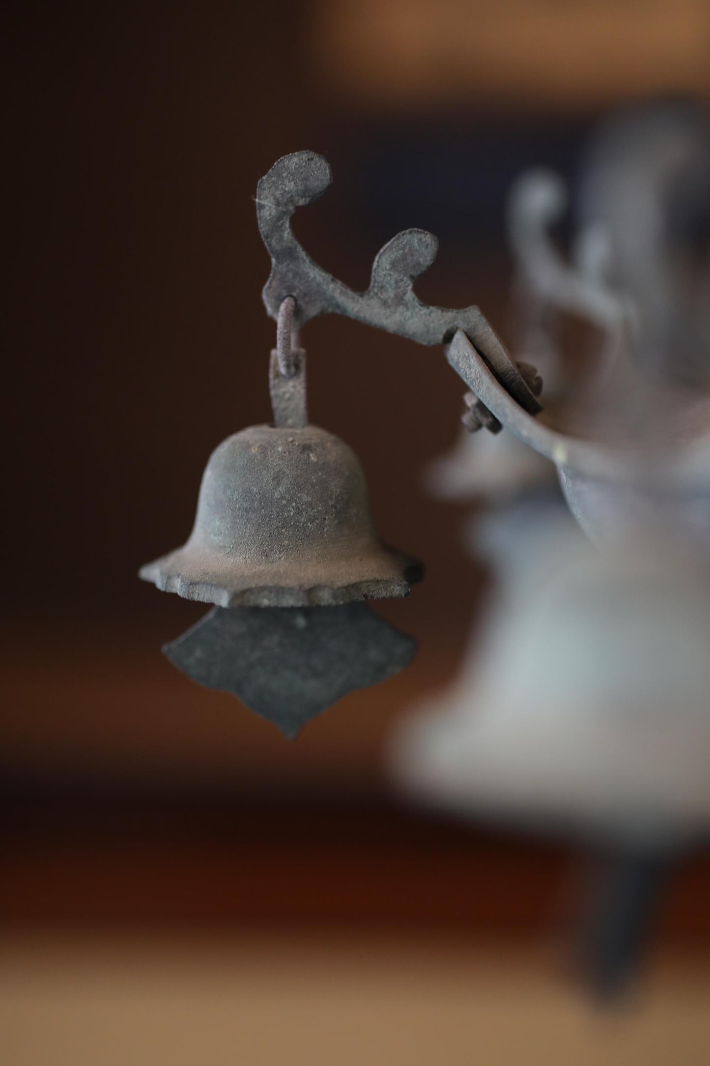 A close-up view of a metal bell or ornament with a textured surface, hanging from a branch or stem.
