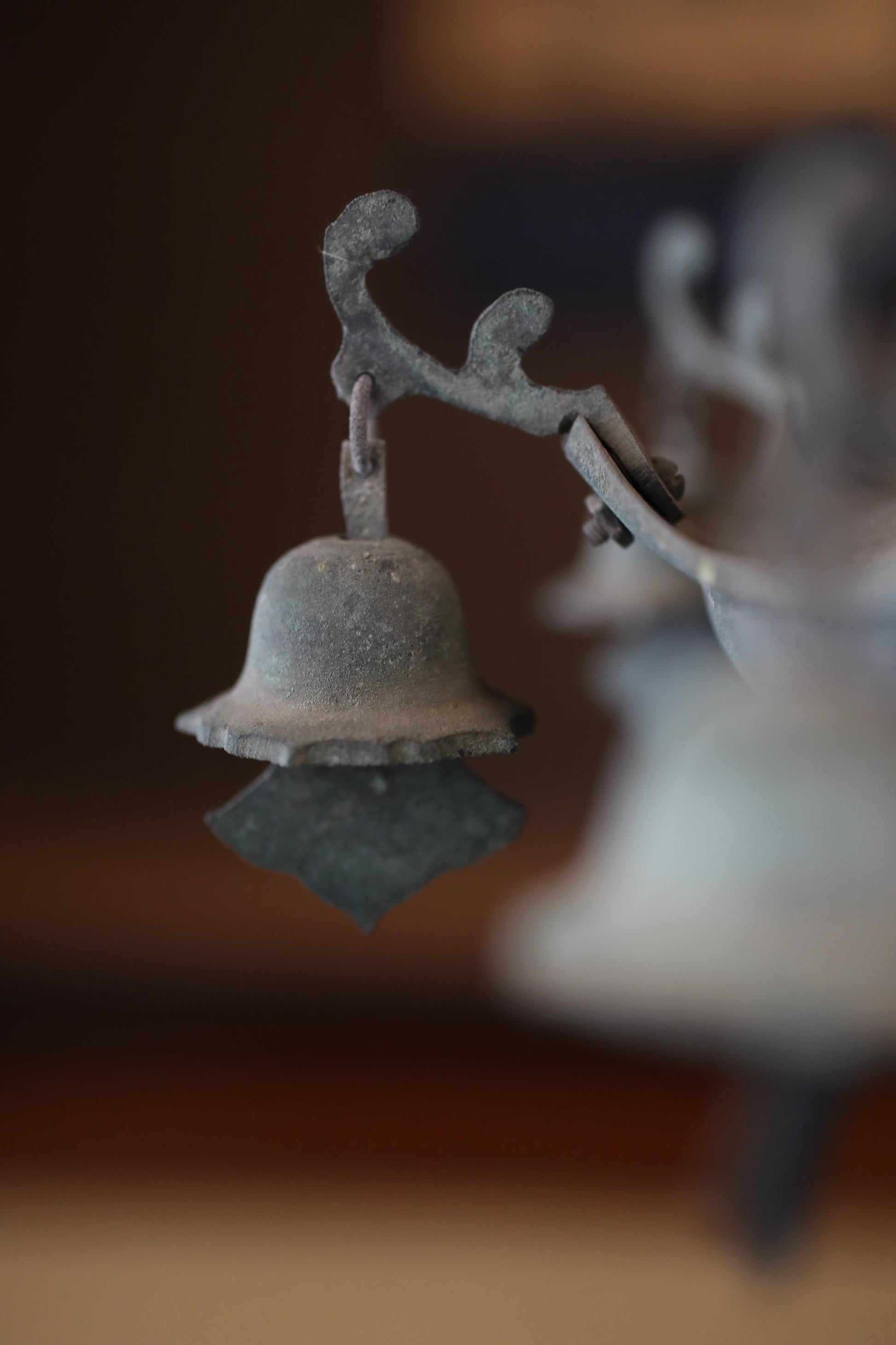 A close-up view of a metal bell or ornament with a textured surface, hanging from a branch or stem.