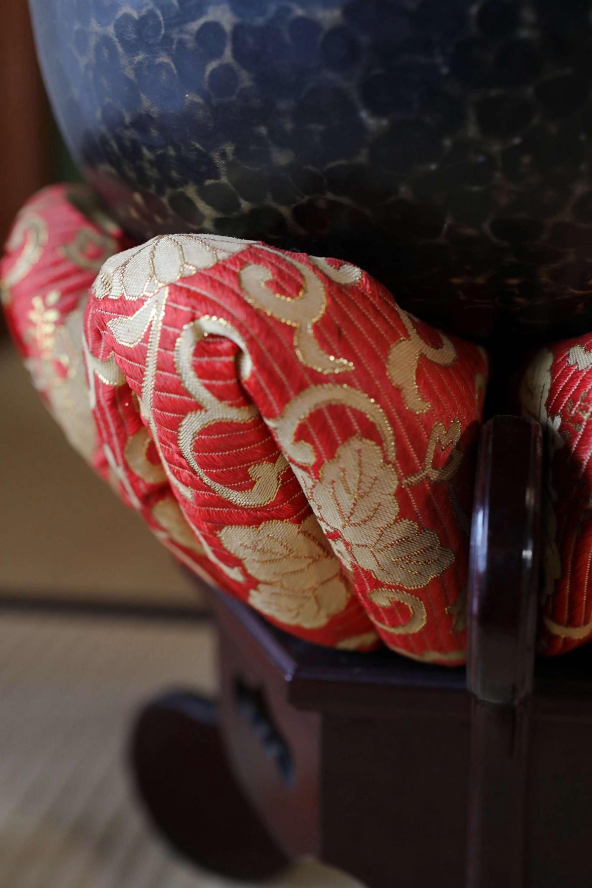 A close-up view of a decorative red and gold fabric with a floral pattern, resting on a dark wooden surface.