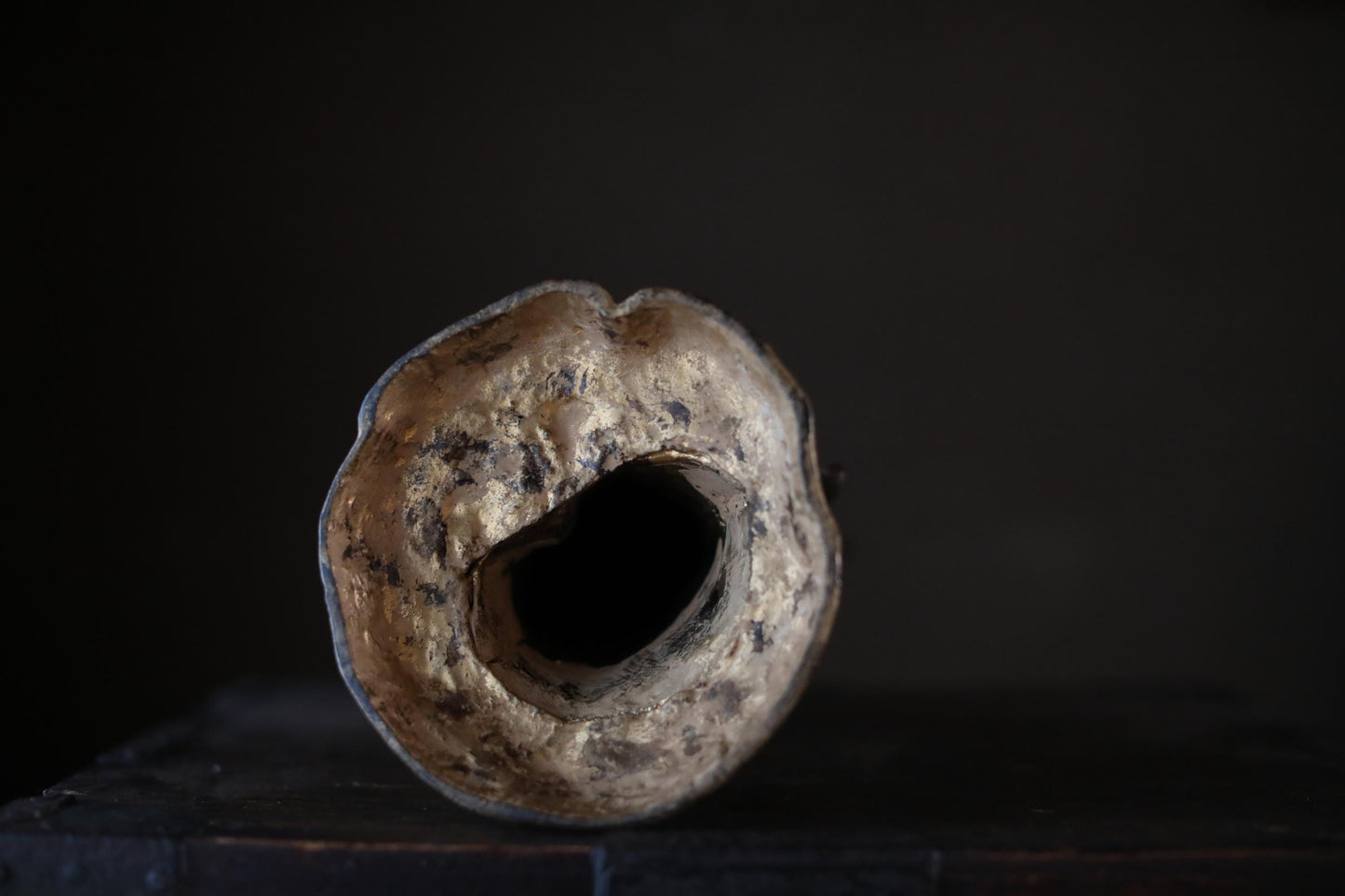 A weathered, circular object with a hole in the center, sitting on a dark surface against a dark background.