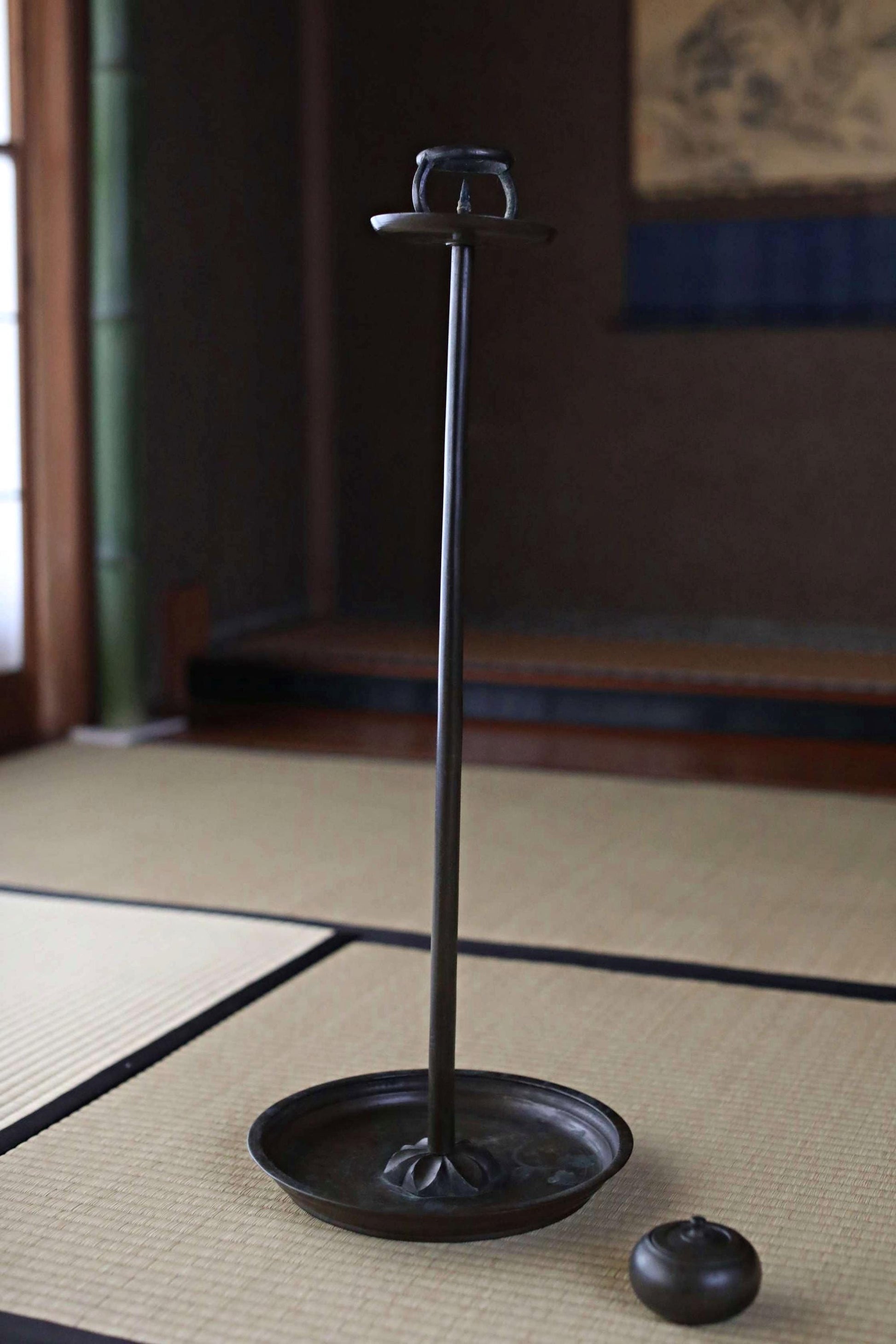 a black metal candlestick holder with a round base and a small black candle holder on the floor.