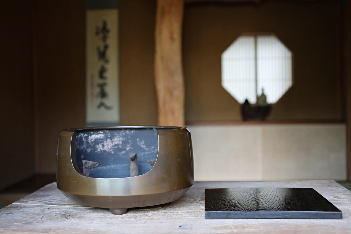 a traditional Japanese tea ceremony setup, including a tea bowl with a wooden base, a black tray, and a window with a white screen.