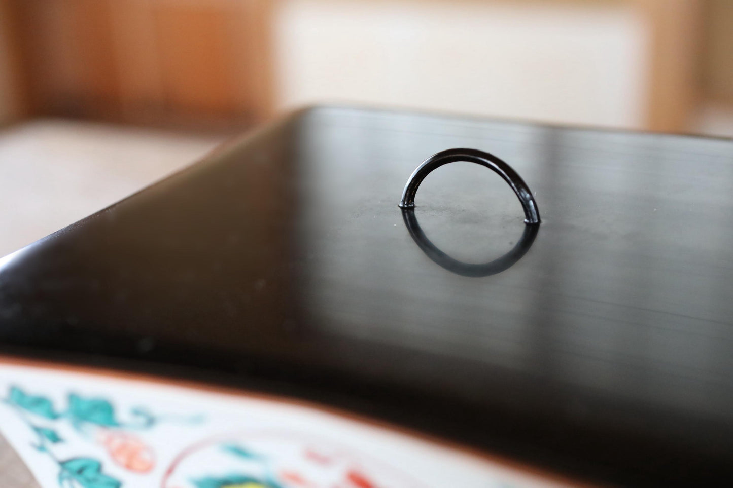 A black metal ring is centered on a black surface, reflecting the surrounding environment.