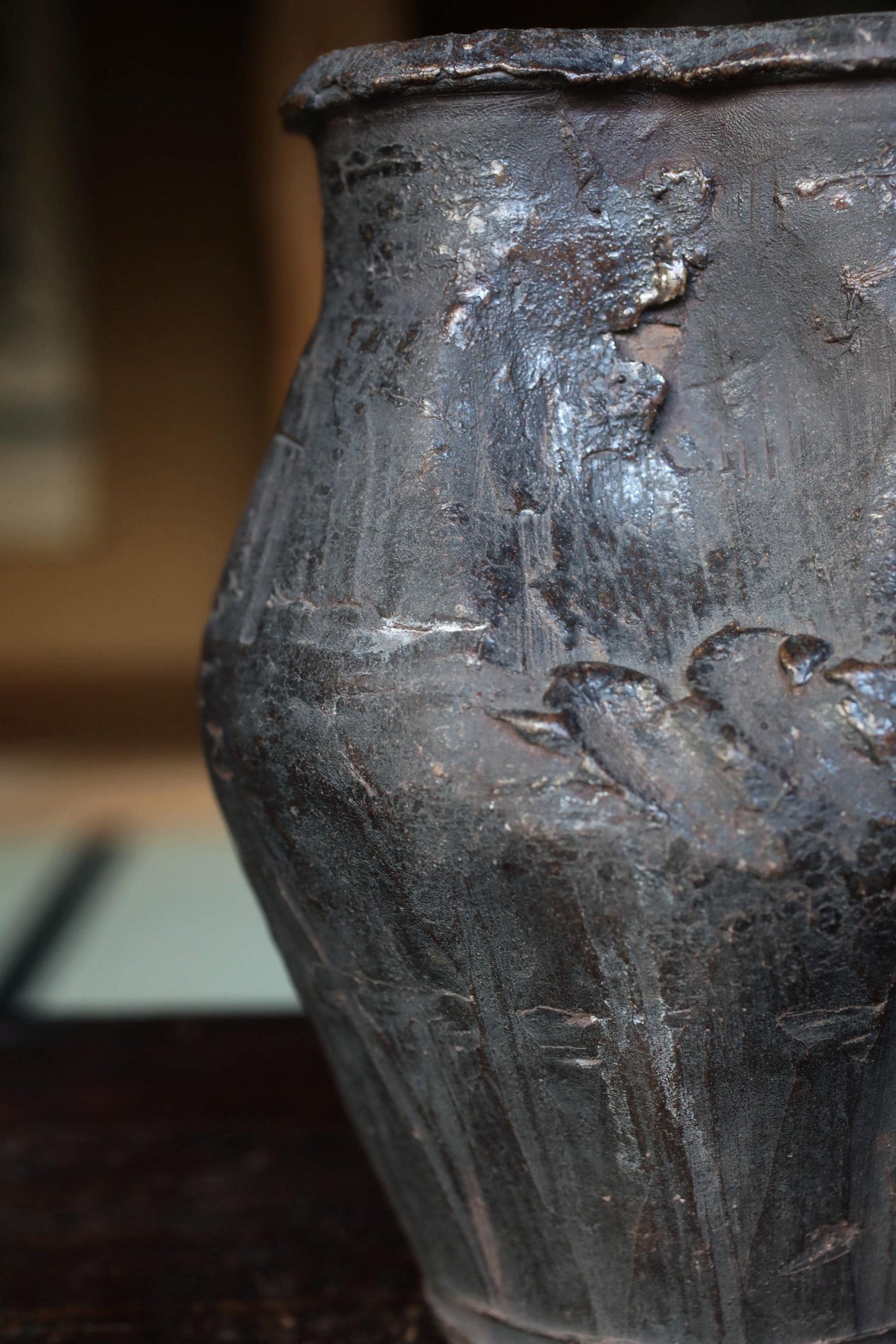 A close-up view of an old, weathered vase with a dark, textured surface.