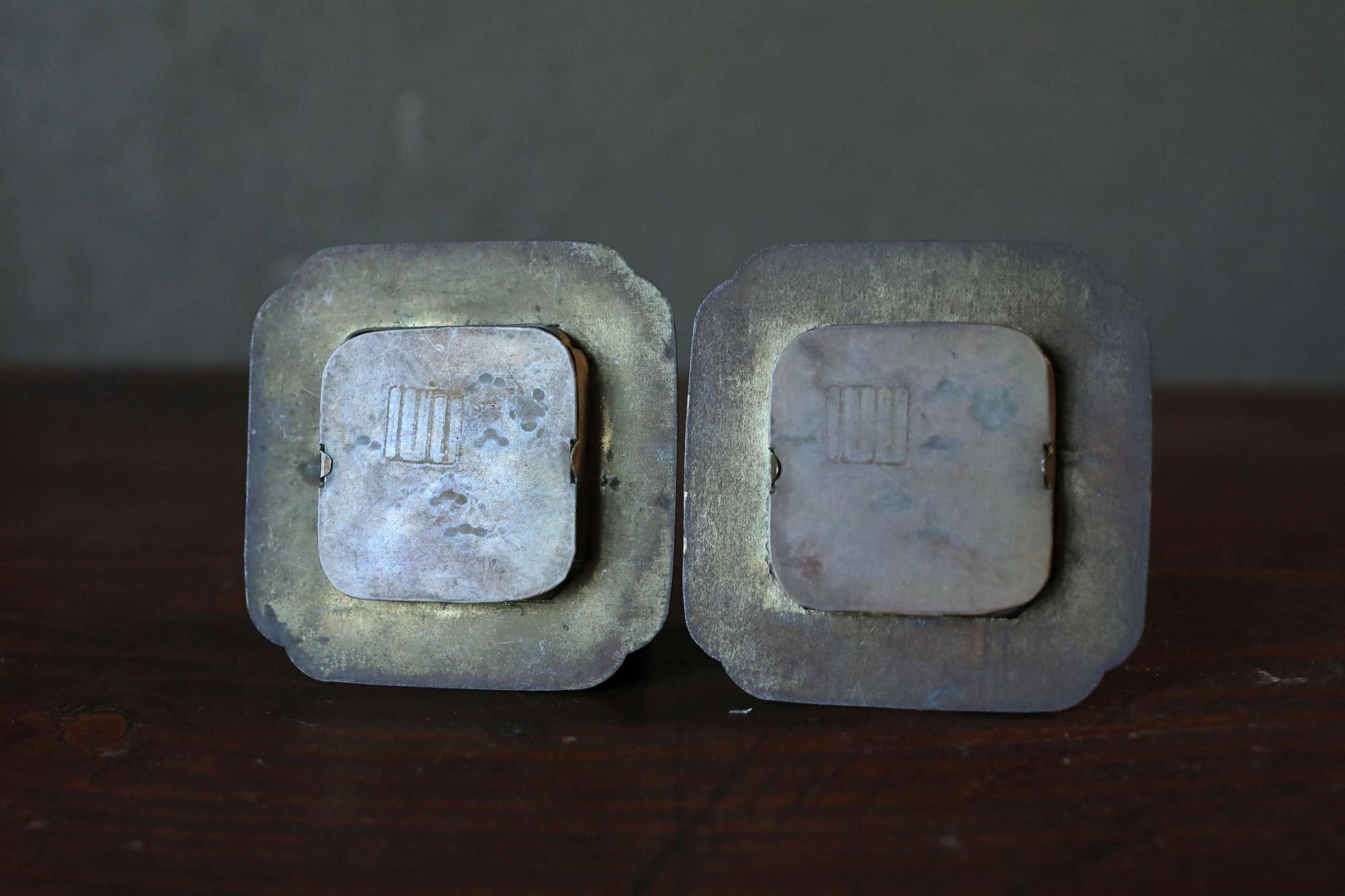 Two old, rusted metal objects with a square shape and a circular cutout in the center, sitting on a wooden surface.