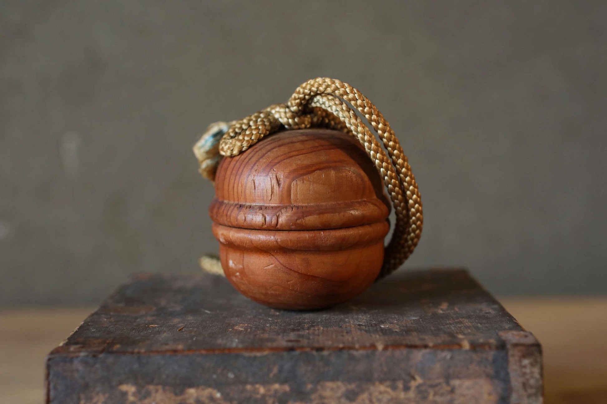 A wooden ball with a gold rope hanging from it, placed on a wooden surface.