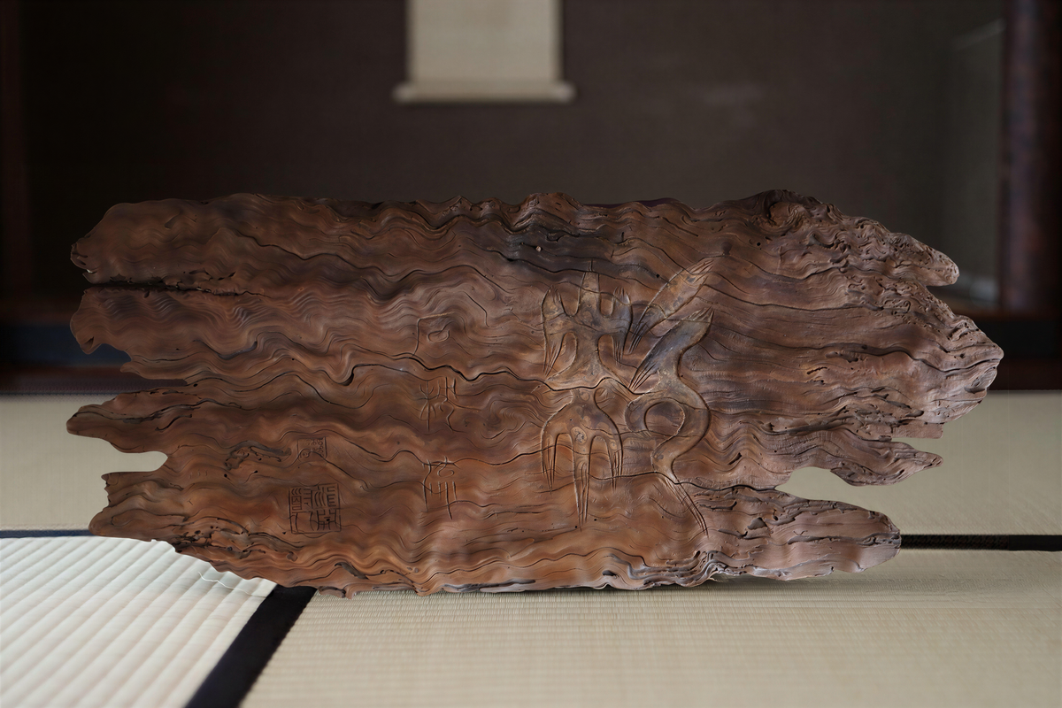 a wooden sculpture with a carved design on its surface, placed on a white mat.