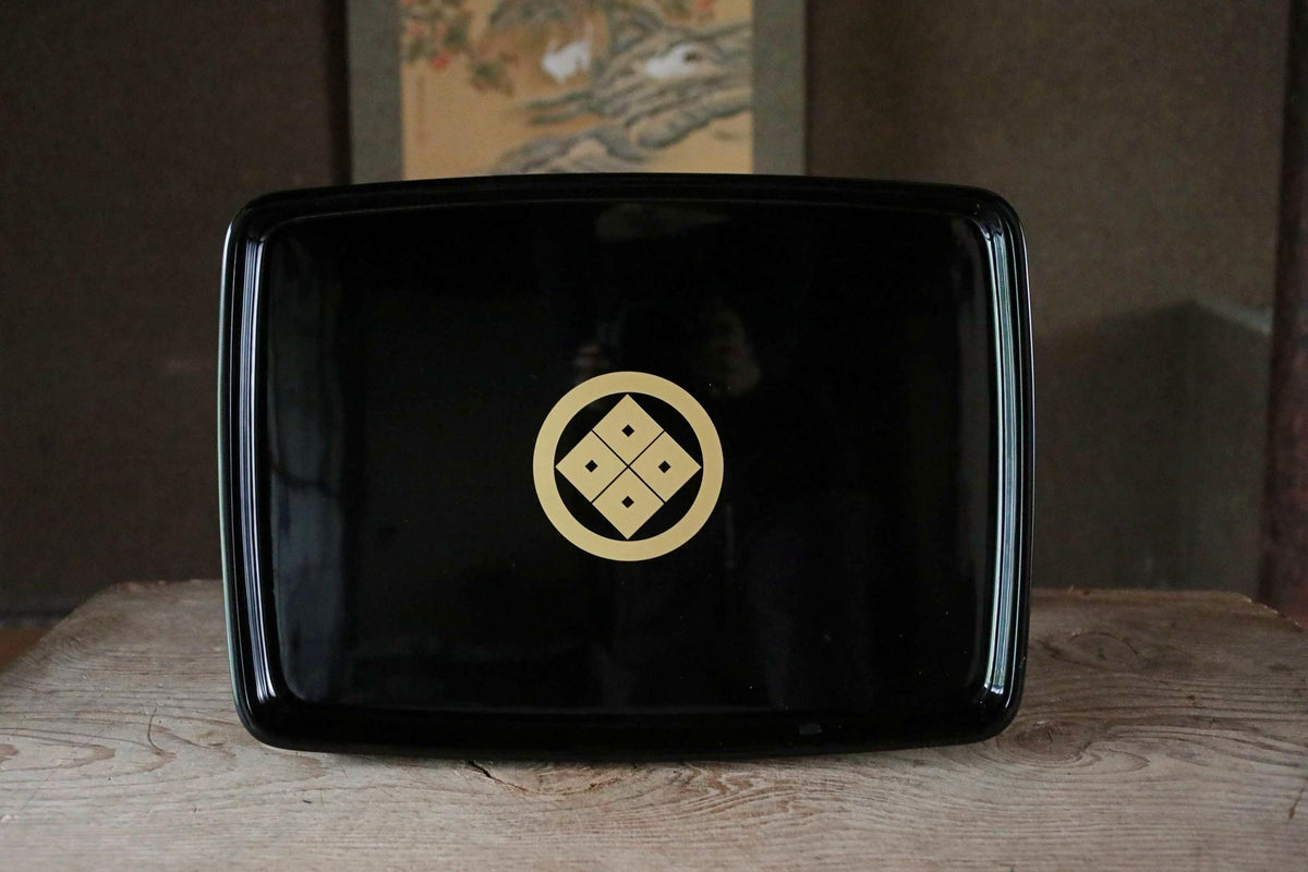A black rectangular tray with a gold emblem on it, placed on a wooden surface.