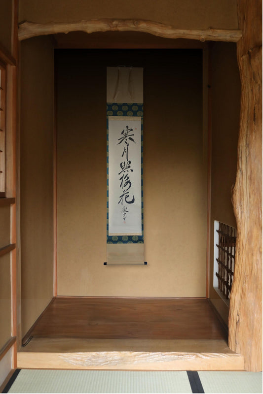 a traditional Japanese room with a wooden floor and a wooden wall. There is a vertical banner hanging on the wall with Japanese characters.