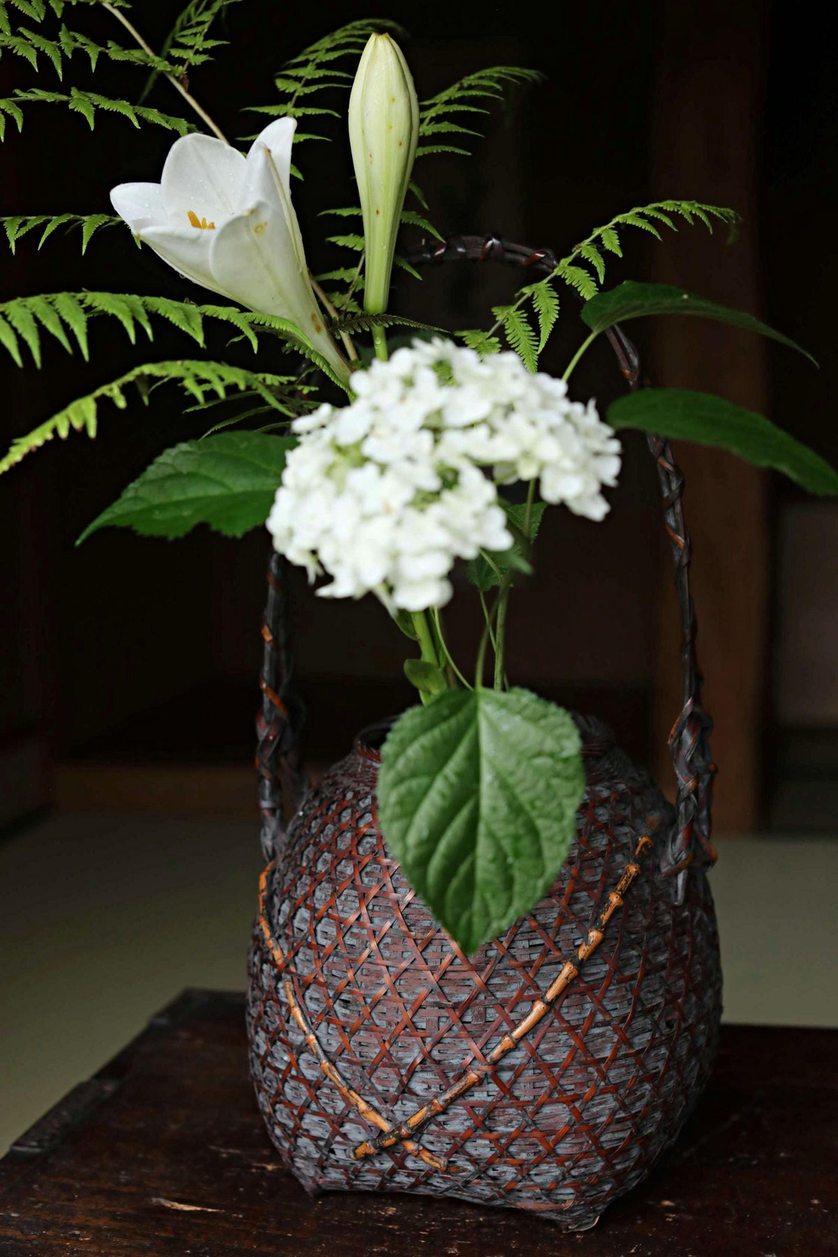 A vase filled with white flowers and green leaves sits on a wooden surface, creating a serene and natural atmosphere.