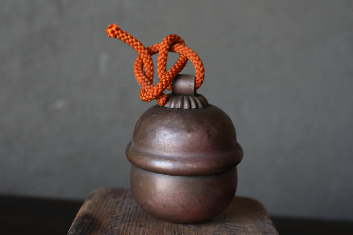 A round, metallic object with a rope tied around it, placed on a wooden surface against a gray background.