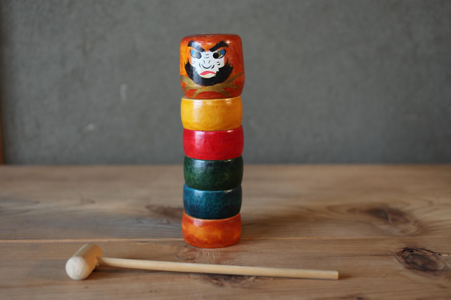 A stack of colorful wooden rings on a wooden surface, with a wooden mallet resting on the ground next to them.