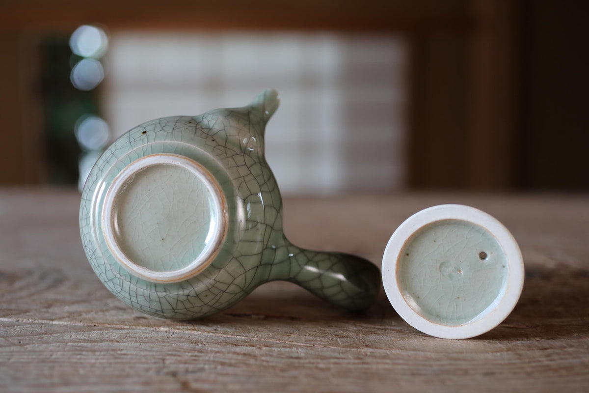 A ceramic teapot with a green and white color scheme is placed on a wooden surface, with the lid of the teapot visible.