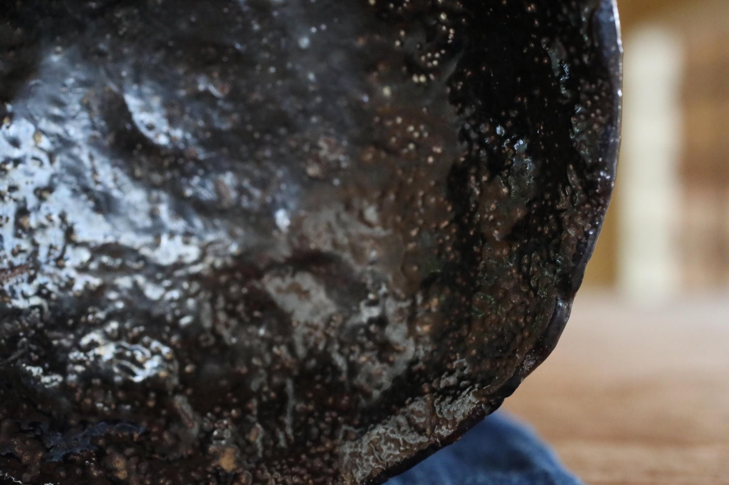 A close-up view of a dark, textured surface with a speckled or speckled appearance, possibly a piece of pottery or a metal object.