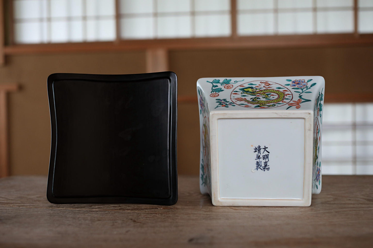 a black square object and a white square object with a decorative design on the back, placed on a wooden surface.
