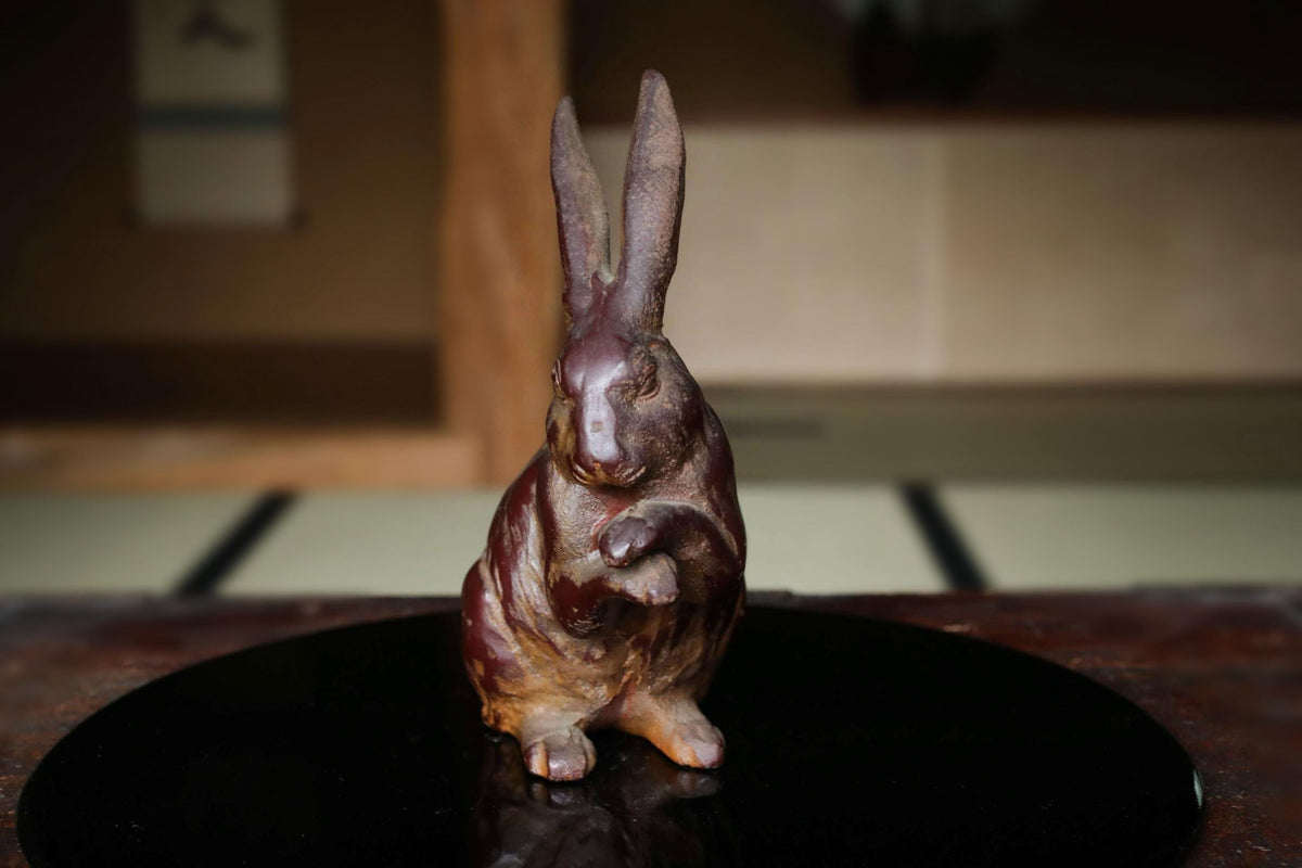 A bronze statue of a rabbit sitting on a black surface.