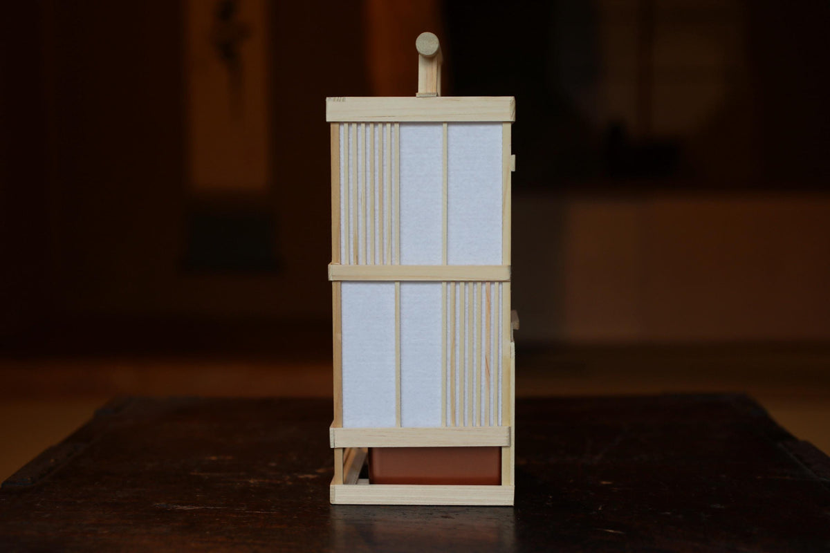 A wooden lantern with a white paper covering is displayed on a dark wooden surface.