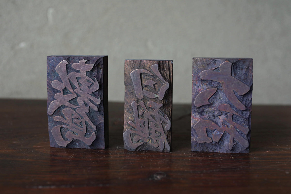 Three rectangular metal blocks with intricate engraved designs on them, placed on a wooden surface.