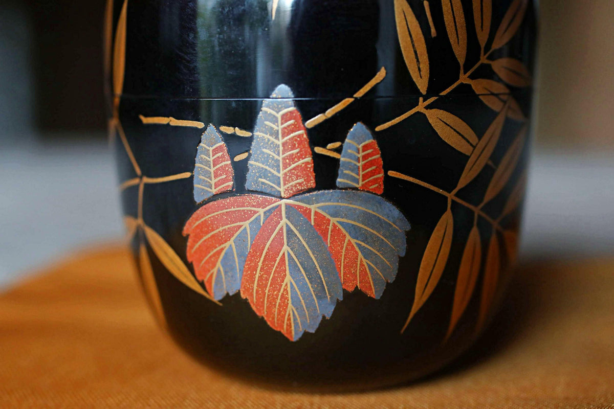 A close-up image of a black vase with a colorful floral design on it, featuring red and blue leaves and branches.
