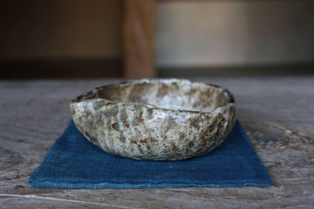 A weathered ceramic bowl sits on a blue cloth on a wooden surface.