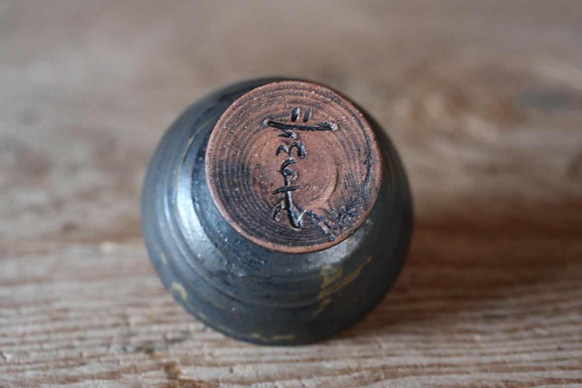 A close-up image of a dark-colored ceramic object, possibly a vase or bowl, with a circular design or inscription on its surface.