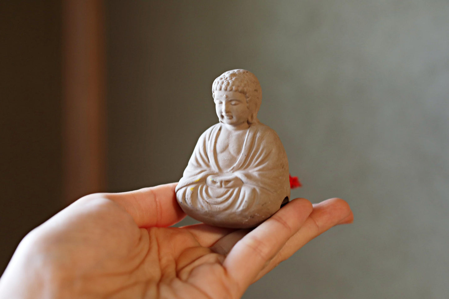 A small white Buddha statue is being held in a person's hand against a blurred background.