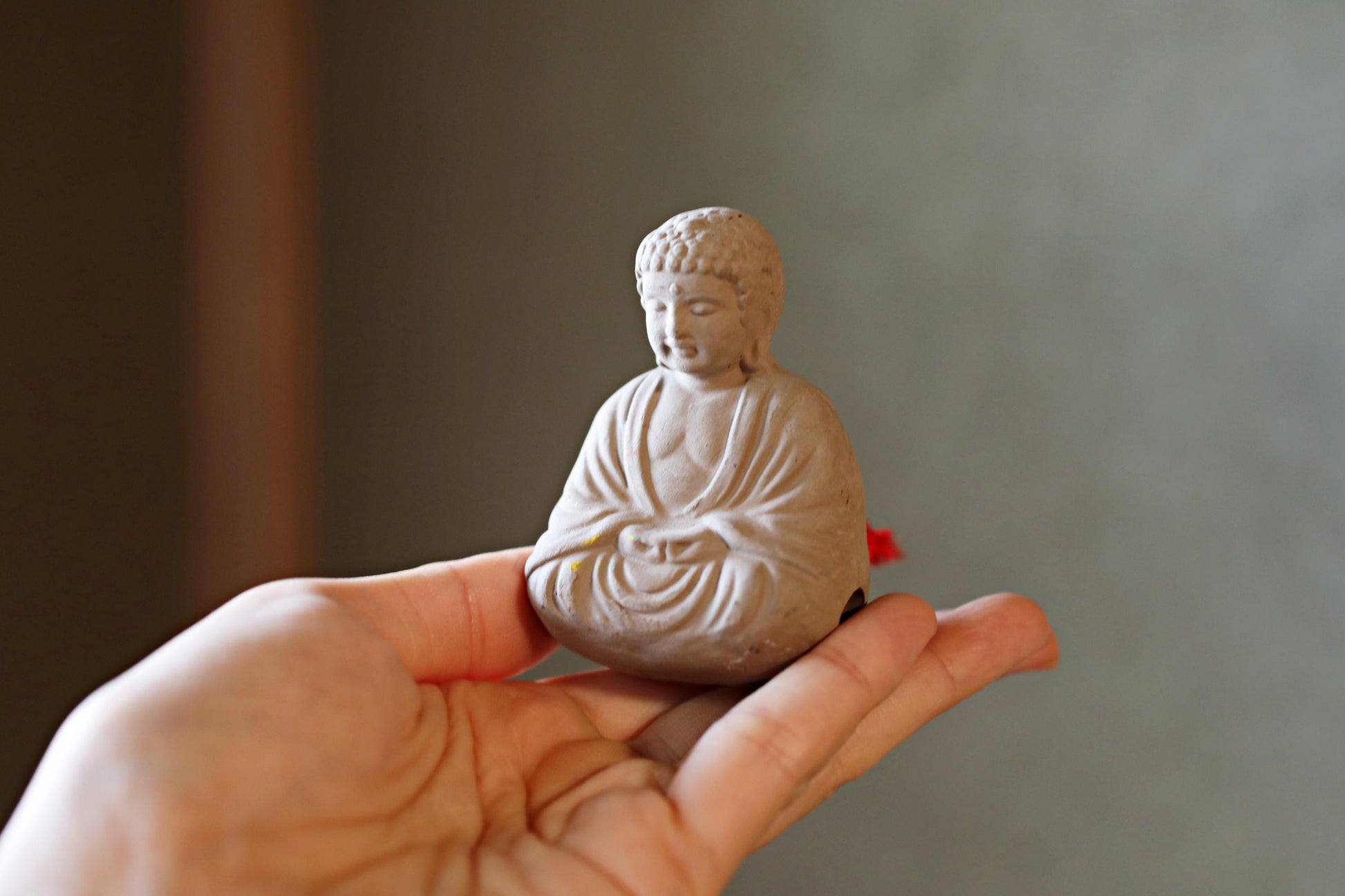A small white Buddha statue is being held in a person's hand against a blurred background.