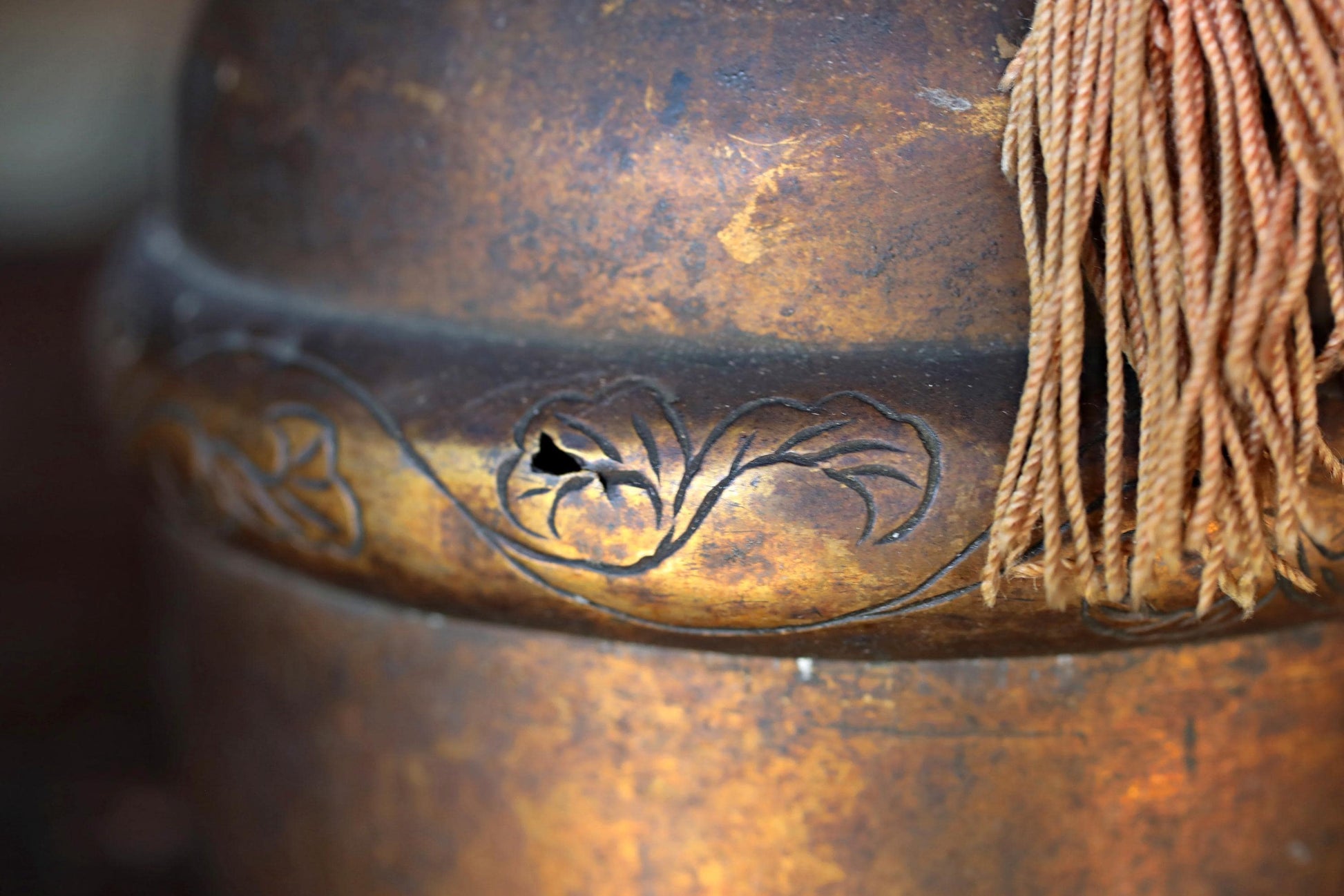 a close-up view of a rusted metal surface with a decorative design, including a tassel hanging from the edge.