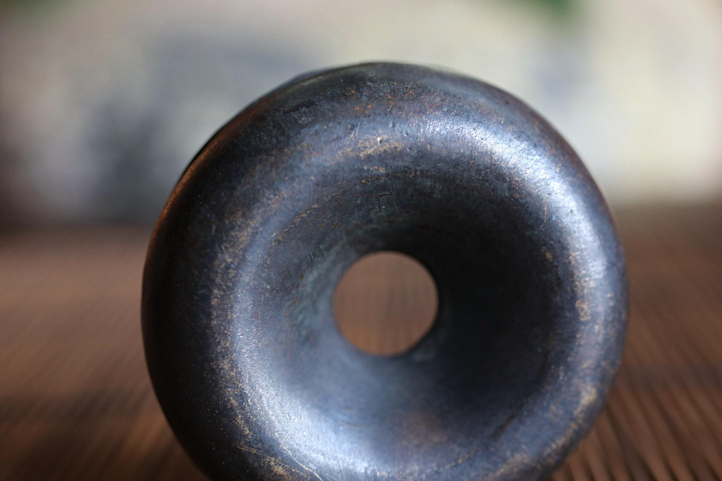 A close-up view of a black, textured object with a circular opening in the center, sitting on a wooden surface.