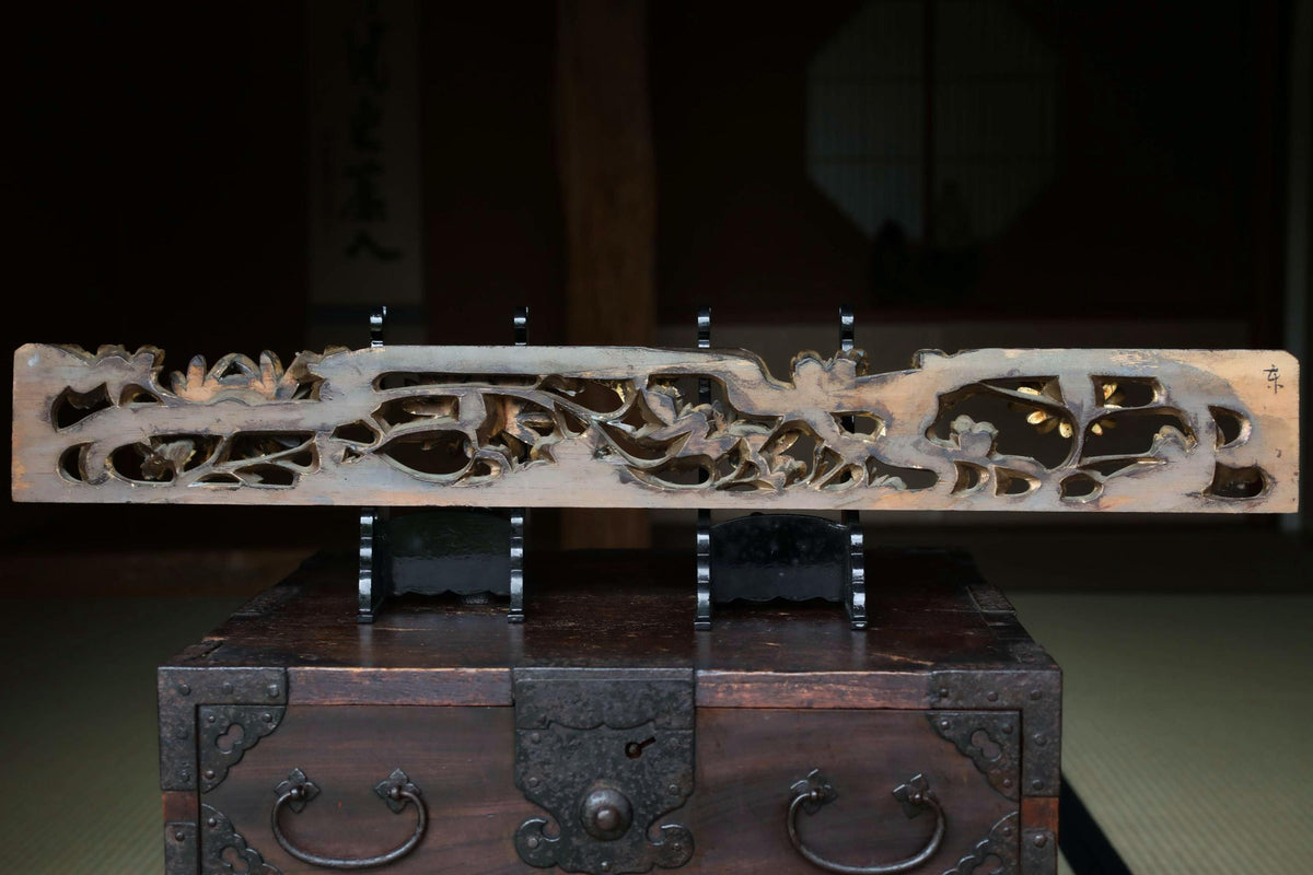 a wooden box with a carved design on its surface, placed on a wooden stand.