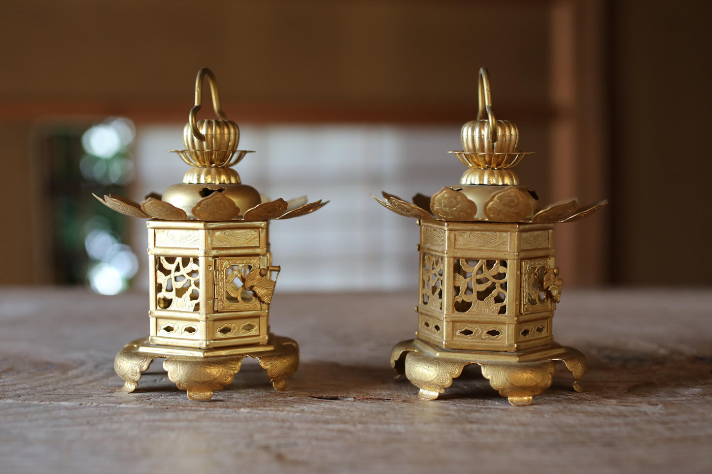 Two ornate golden lanterns with intricate designs are displayed on a wooden surface.