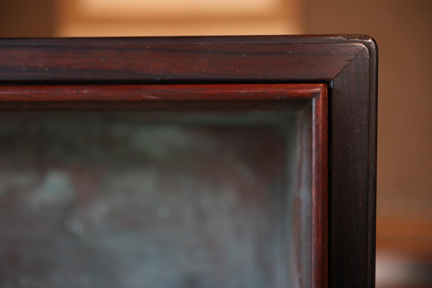a close-up view of a dark wooden frame with a glass or metal component inside, possibly a window or a display case.