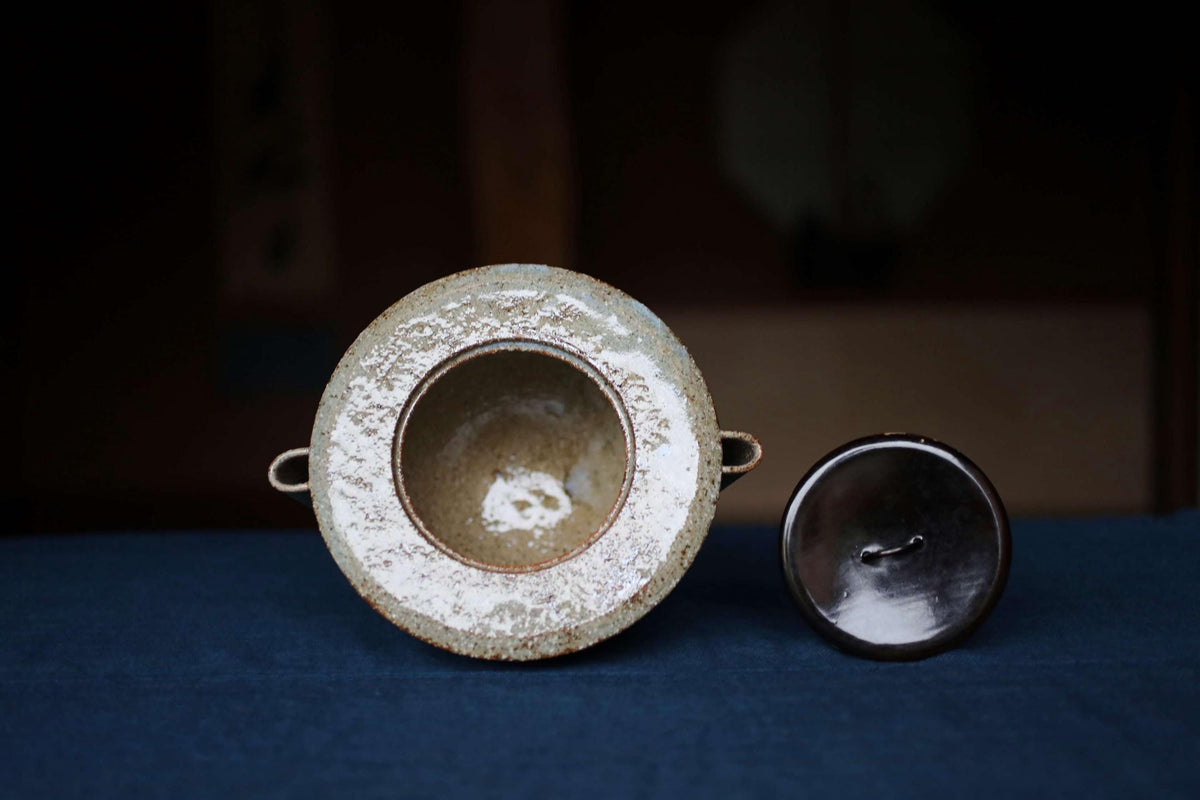 a ceramic container with a white interior and a black exterior, placed on a blue surface.