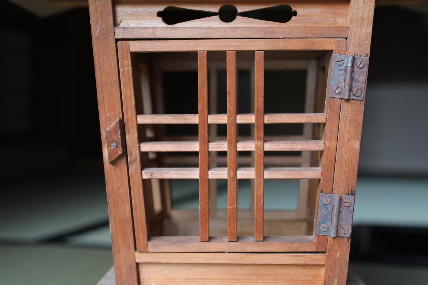 A close-up view of a wooden structure with a lattice-like design, featuring a small window and metal hinges.