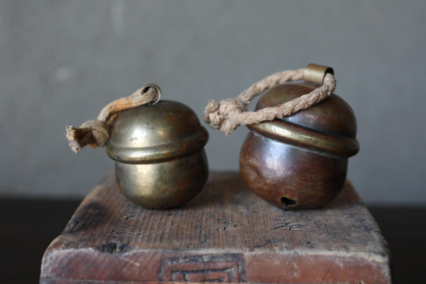Two antique brass bells with rope handles are displayed on a wooden surface.