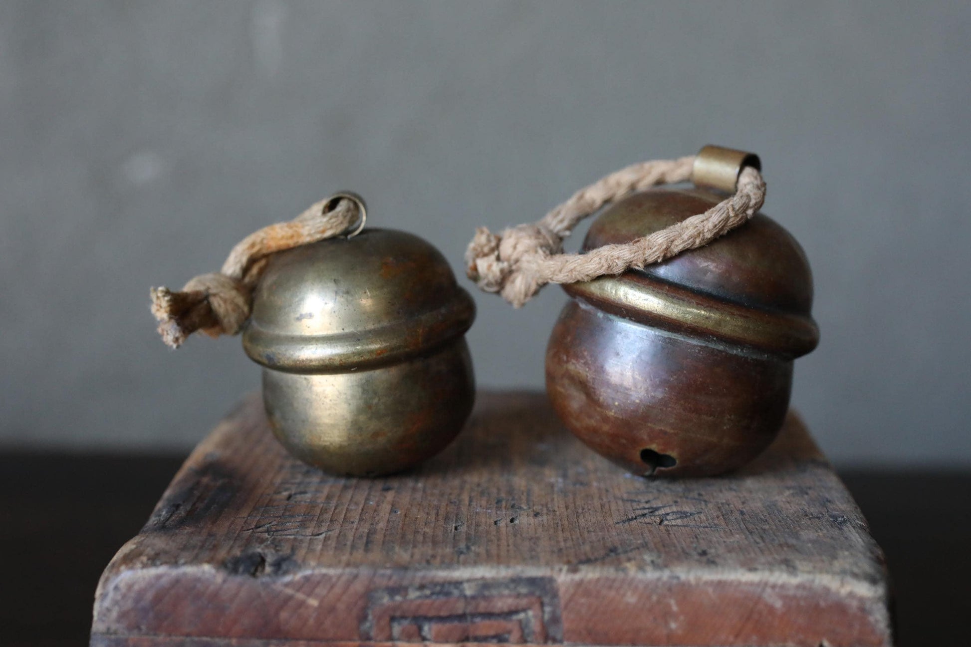 Two antique brass bells with rope handles are displayed on a wooden surface.
