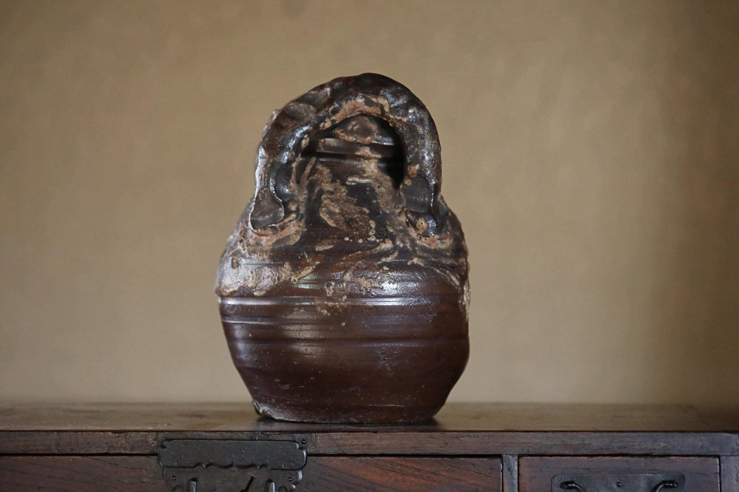 An old, dark brown ceramic vase with a unique, twisted shape sits on a wooden surface.